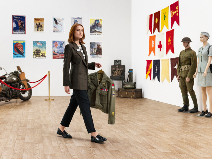 Una mujer con ropa de oficina cargando una chaqueta militar en un museo