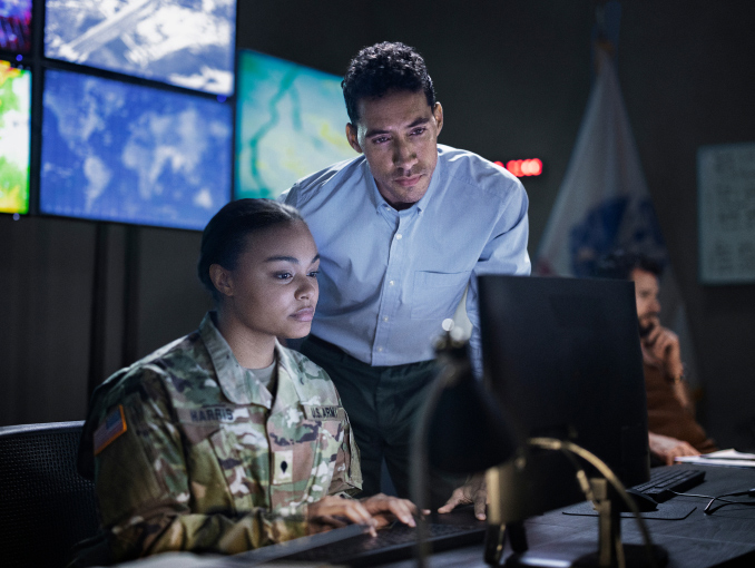 Un hombre en ropa casual de negocios mirando la pantalla de una computadora con una Soldado en uniforme de combate